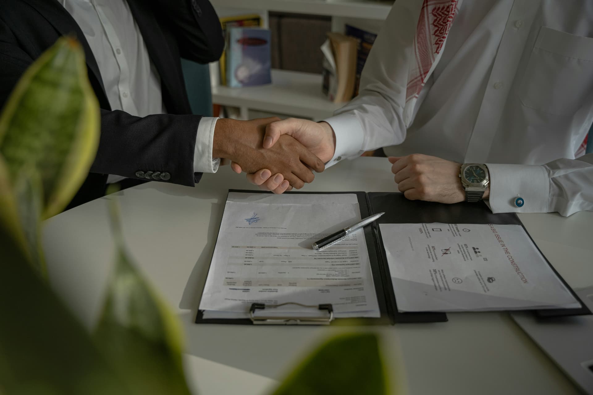 Two business professionals shaking hands over a signed agreement at a desk